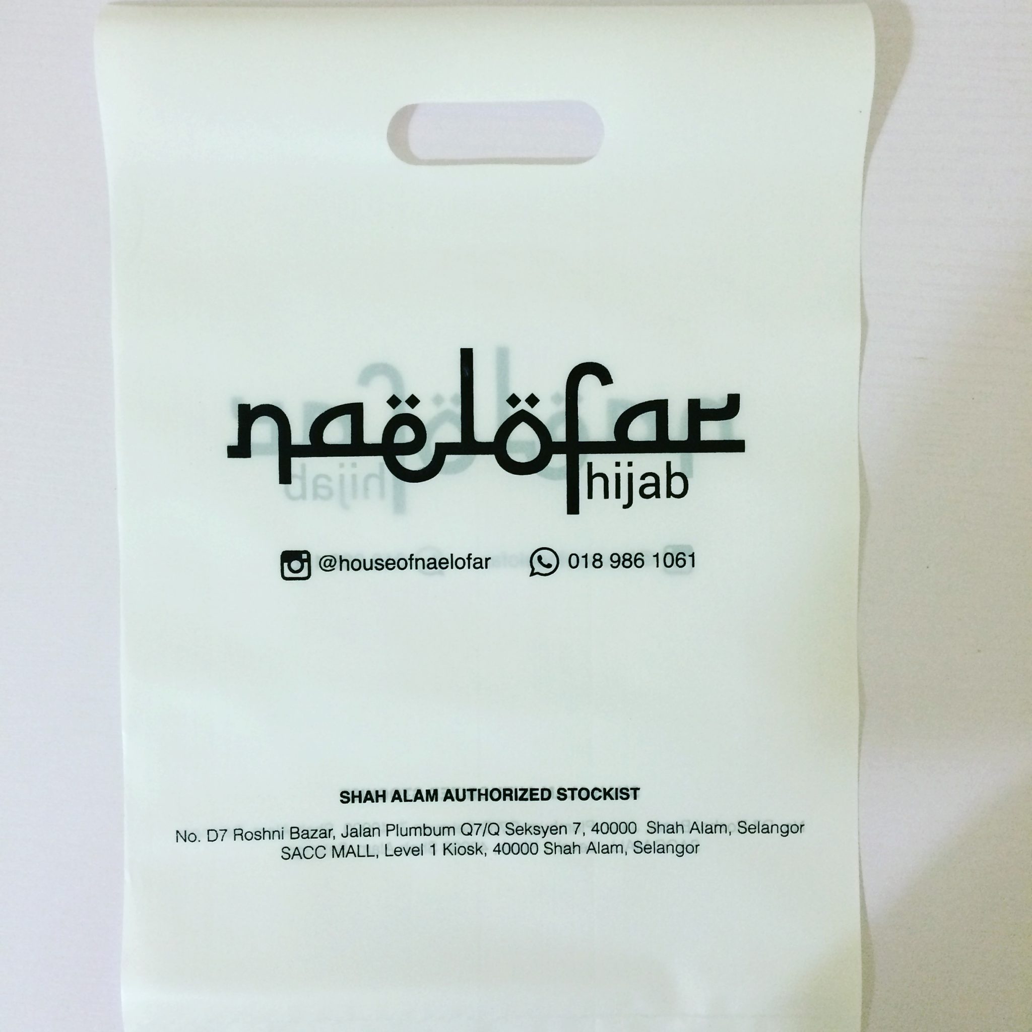 White retail carrier bag with a die-cut handle and printed contact details on the front