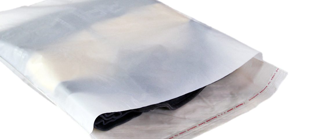 A clear poly mailer bag containing folded clothing items, with the flap open to reveal the contents and a red printed sealing strip.