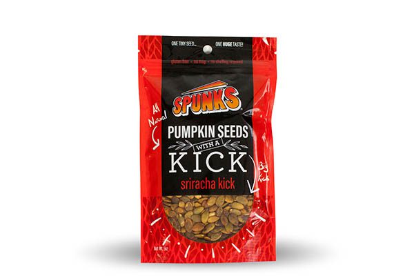 A red and black stand-up pouch filled with pumpkin seeds. The pouch has a resealable top and features prominent text indicating "Pumpkin Seeds with a Kick" and "Sriracha Kick."