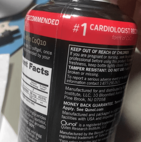 The image shows a hand holding a bottle of CoQ10 supplements, with the focus on the label and the label's background. * The bottle