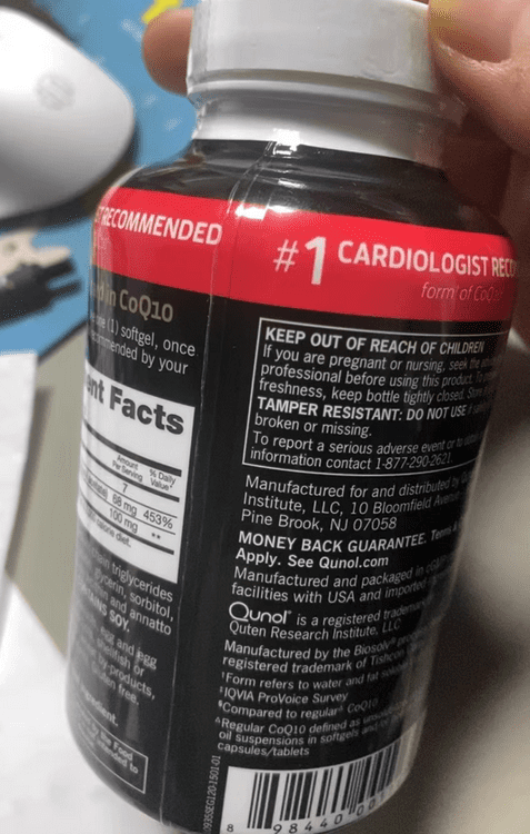 The image shows a hand holding a bottle of CoQ10 supplements, with the focus on the label and the label's background. * The bottle