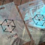 Two transparent packaging bags with die-cut handles at the top. Each bag features a black hexagonal logo and the word 'HEXOR' printed in black text below it.