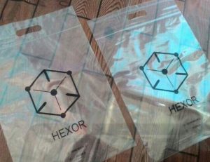 Two transparent packaging bags with die-cut handles at the top. Each bag features a black hexagonal logo and the word 'HEXOR' printed in black text below it.