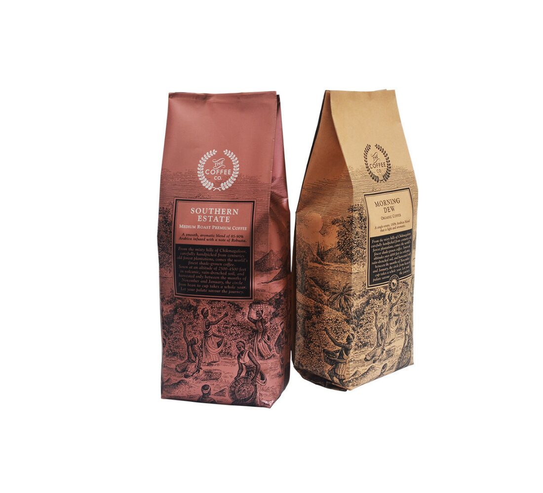 Two upright coffee bags, one rose-gold and one kraft brown, are shown against a white background. Both bags have a folded top closure and feature detailed illustrations and text.