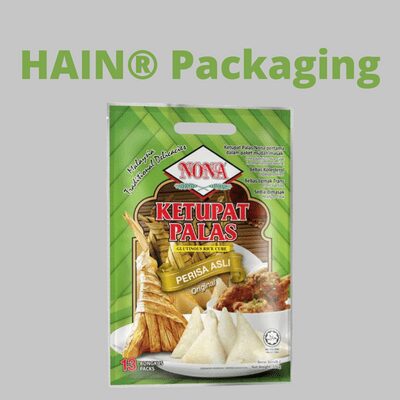 A green and white package for Ketupat Palas, featuring images of the rice cakes and a serving suggestion. The package has a die-cut handle at the top.