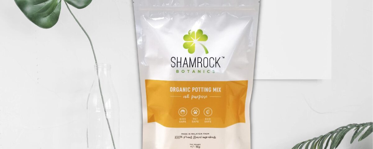 A white and orange resealable pouch containing organic potting mix, with a shamrock logo and text indicating it is for all purposes. Icons for kids, pet, and eco safety are visible.