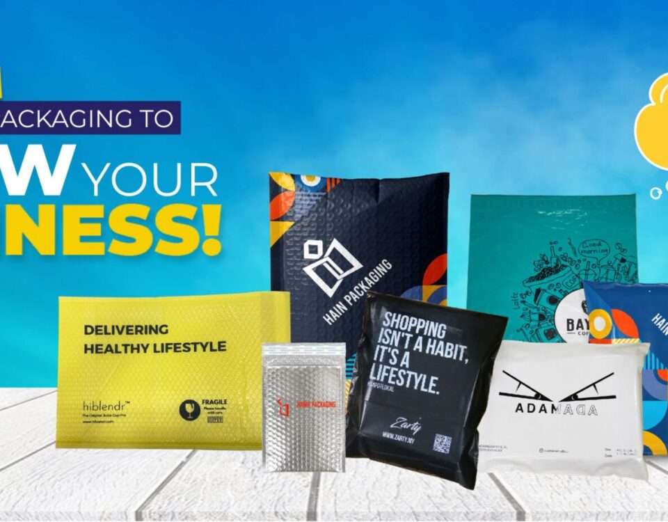 A collection of various mailing envelopes displayed on a white wooden surface against a blue sky background. The envelopes feature different colors, patterns, and printed text, including "GROW YOUR BUSINESS!" and "DELIVERING HEALTHY LIFESTYLE."