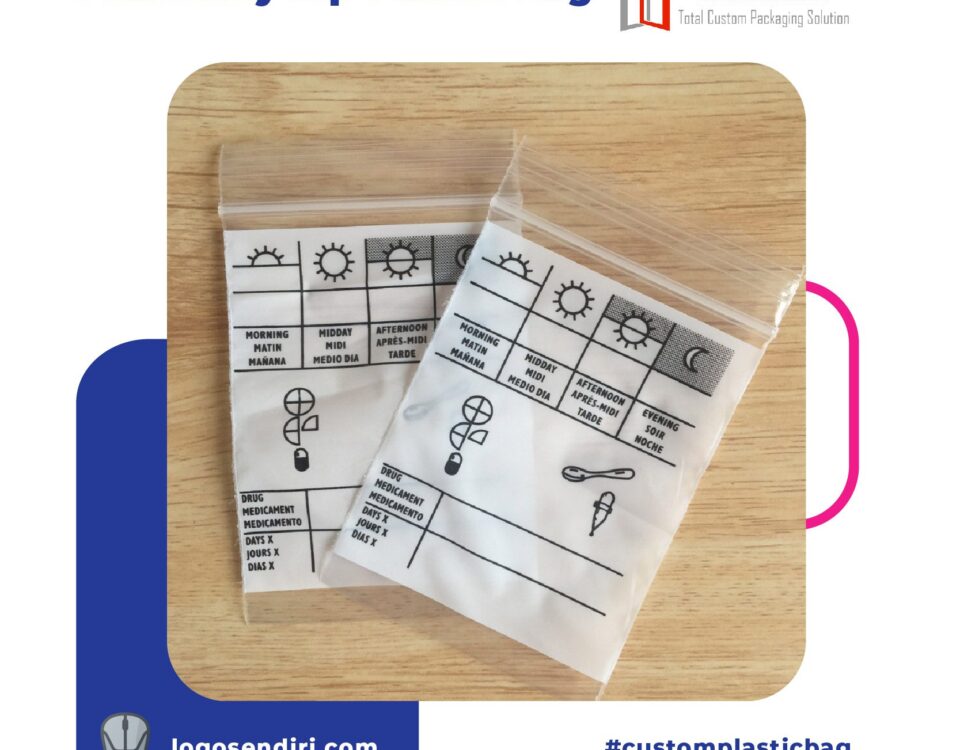 Two clear plastic zip-top bags are shown on a wooden surface. Each bag contains a white insert printed with a grid for tracking medication times (Morning, Midday, Afternoon, Evening) and icons representing drugs, a spoon, and a dropper. Text is printed in multiple languages.