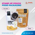 Two stand-up pouches, one white and one gold, with product information and branding. The white pouch displays "SAMBAL HITAM Kaya Dengan Tradisi" and nutritional details. The gold pouch shows "NORAD" branding and nutritional information. A label indicates "16 x 11cm" and "Matte".