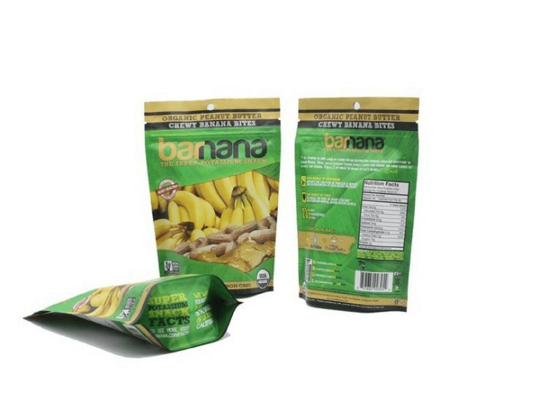 Three green resealable pouches for chewy banana bites, one lying flat and open, showing bananas and peanuts. The other two stand upright, one with a front view and the other with a back view displaying nutrition facts.